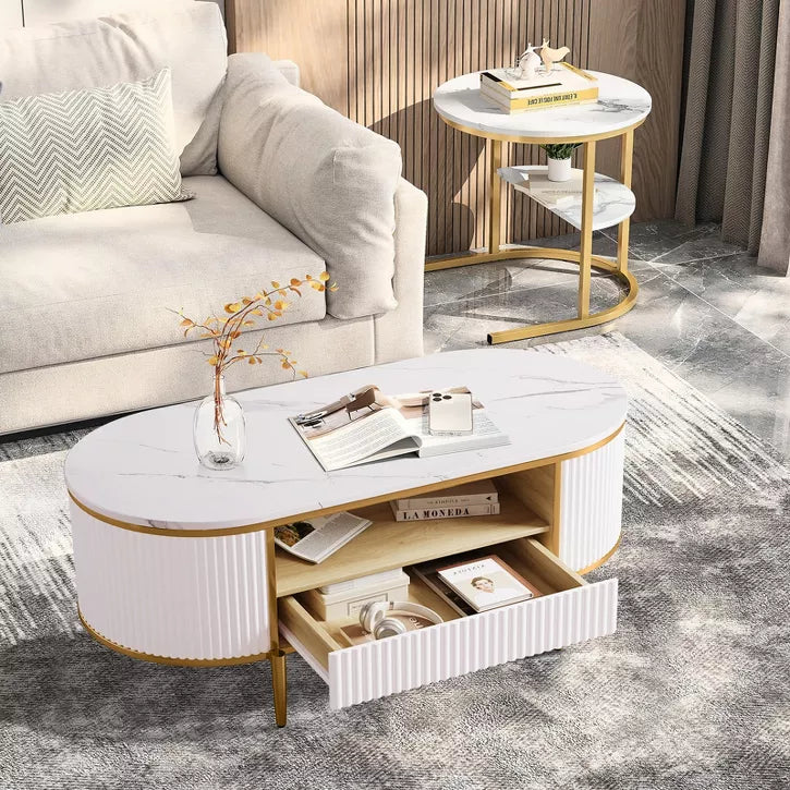 White and gold coffee table with magazines and a vase in a living room setting.