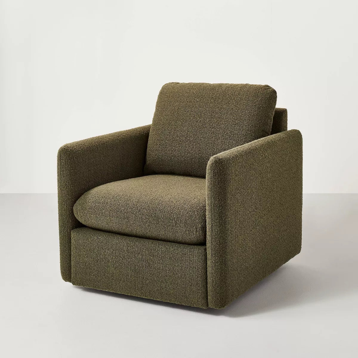 A greenish brown colored armchair with a textured fabric and square shape, placed on a light gray floor.