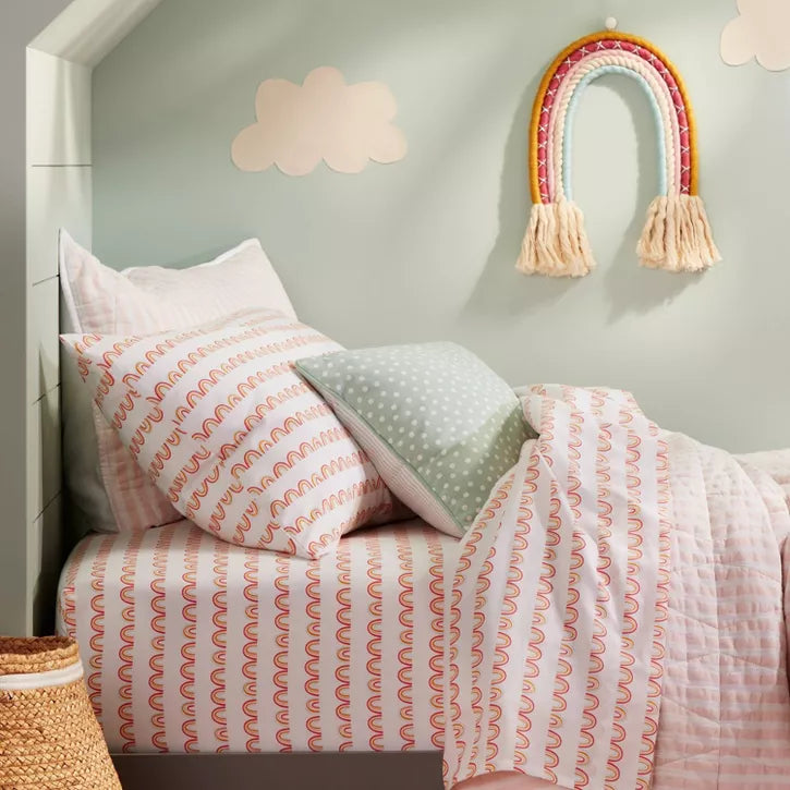 Bedroom with floral bedding and colorful pillows on a bed against a pink wall.