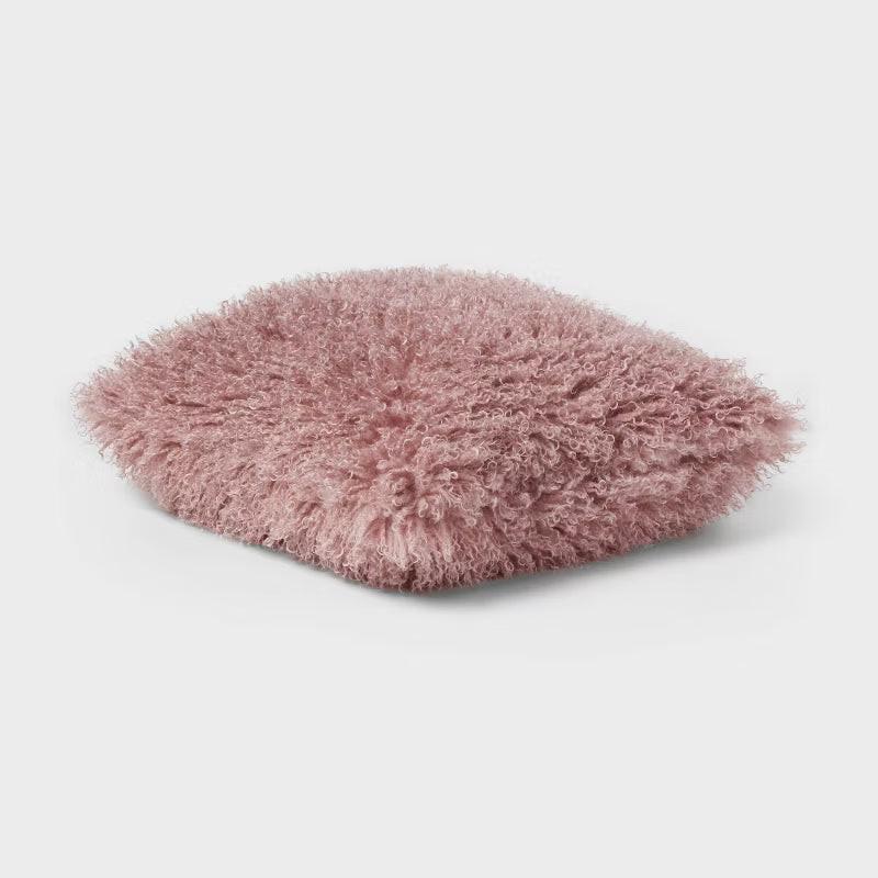 Close-up of a bed with burgundy quilt, pillows, and a fluffy pink pillow. Mauve