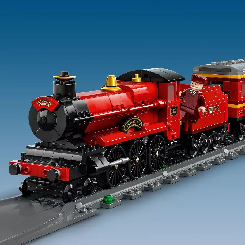 Red toy steam locomotive with engineer figure on tracks against a blue background