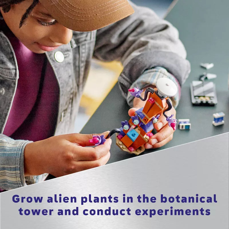 Person holding a small robot-like device with colorful components, sitting at a table.