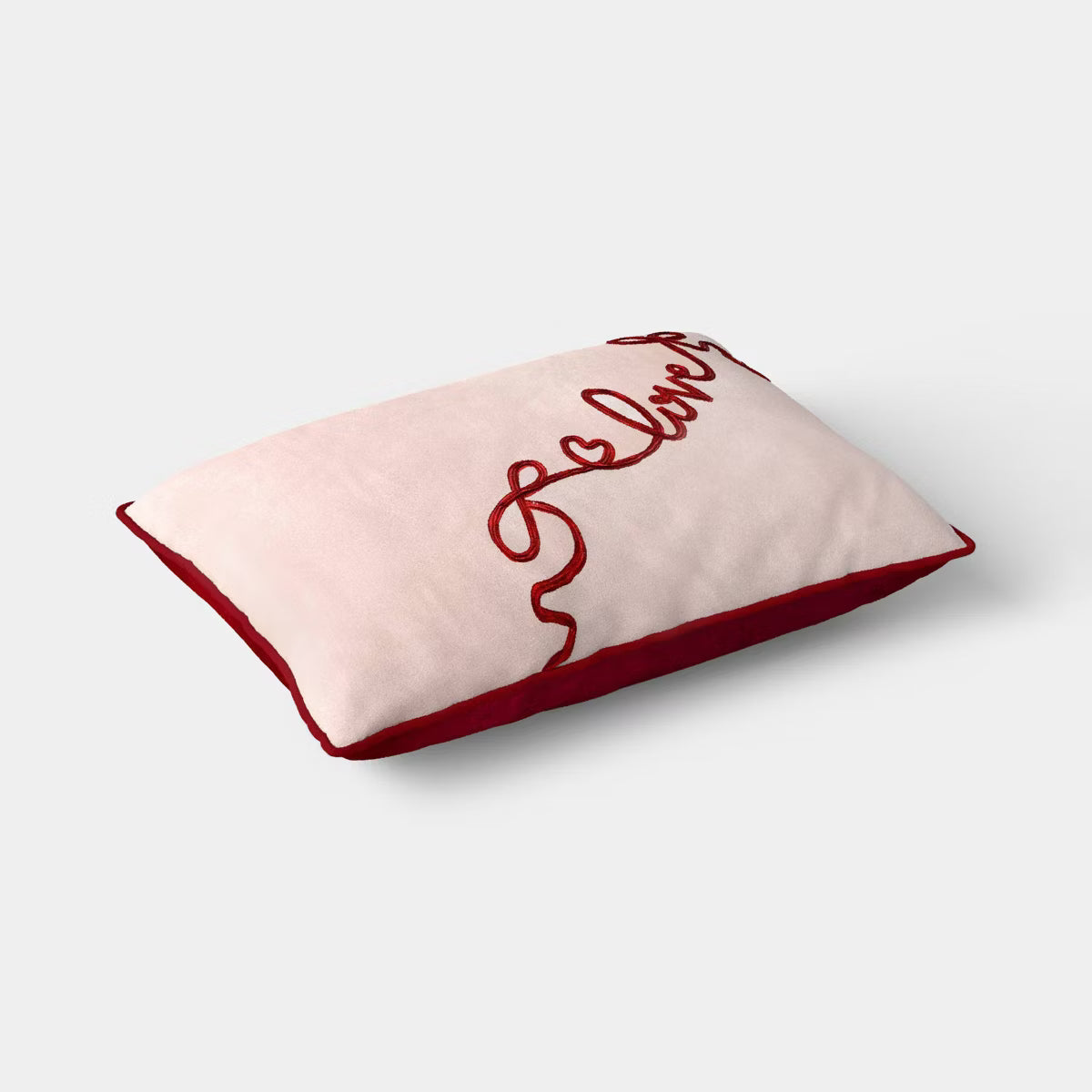 Rectangular light pink colored pillow with red colored piping and the word & quot love quot embroidered in red.