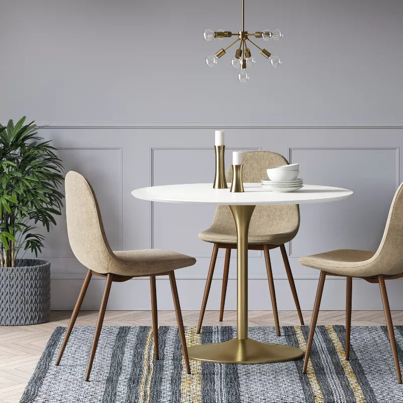 Dining room with a round table and chairs, gold chandelier, and plant on a gray wall background.