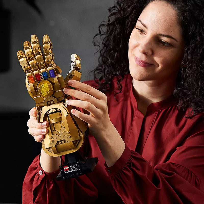 Woman holding a gold LEGO model of a glove with colorful stones against a dark background