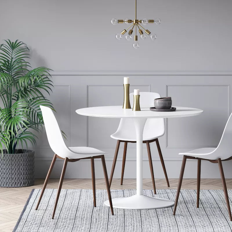 Dining room with a round white table and chairs, potted plant, and chandelier.