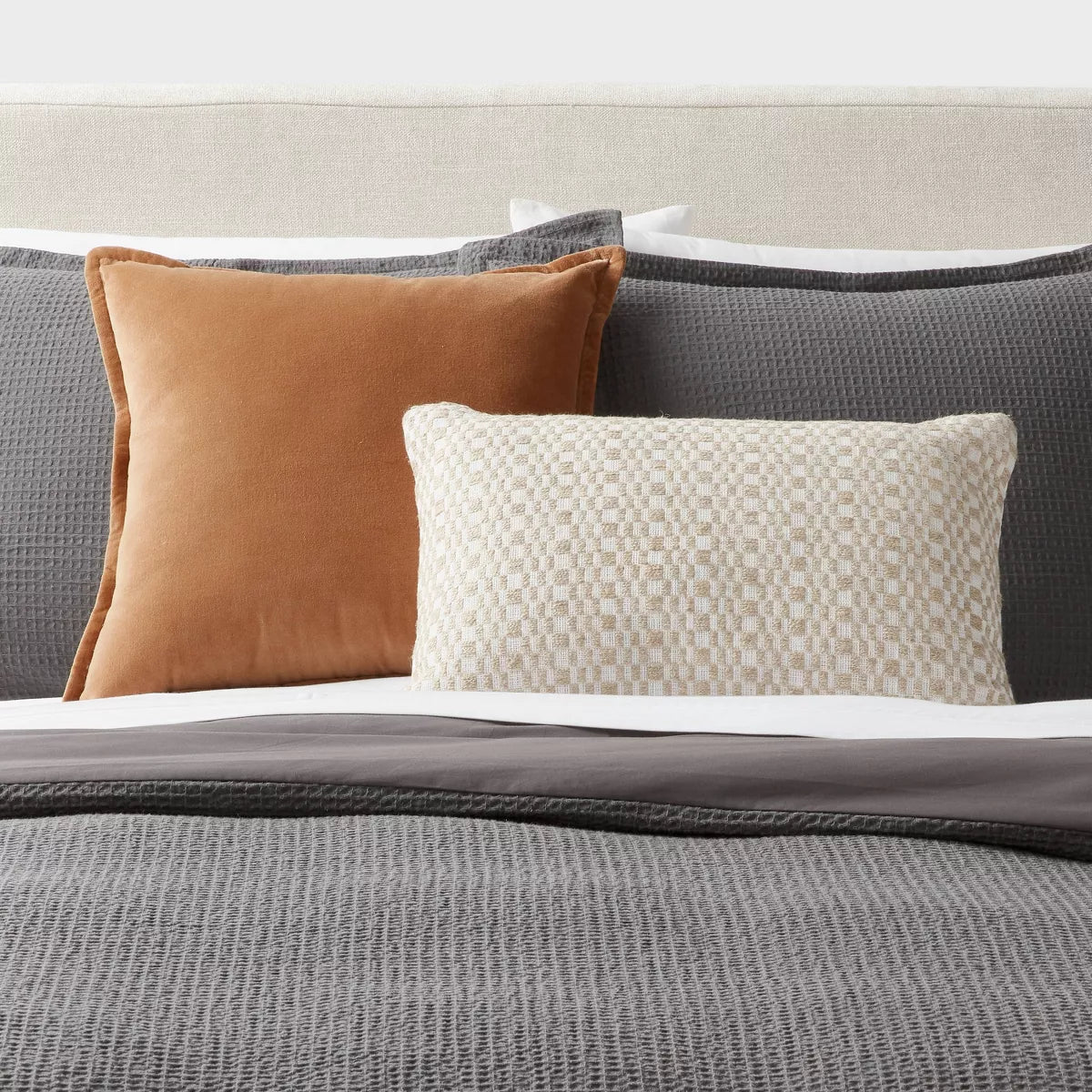 A rectangular throw pillow with a textured woven checkerboard pattern in cream and beige, shown against a light gray background with a soft drop shadow.