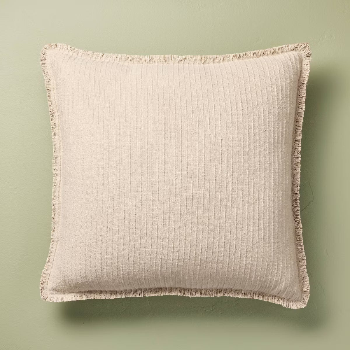 Beige textured pillow with a brand label on a green background Tan