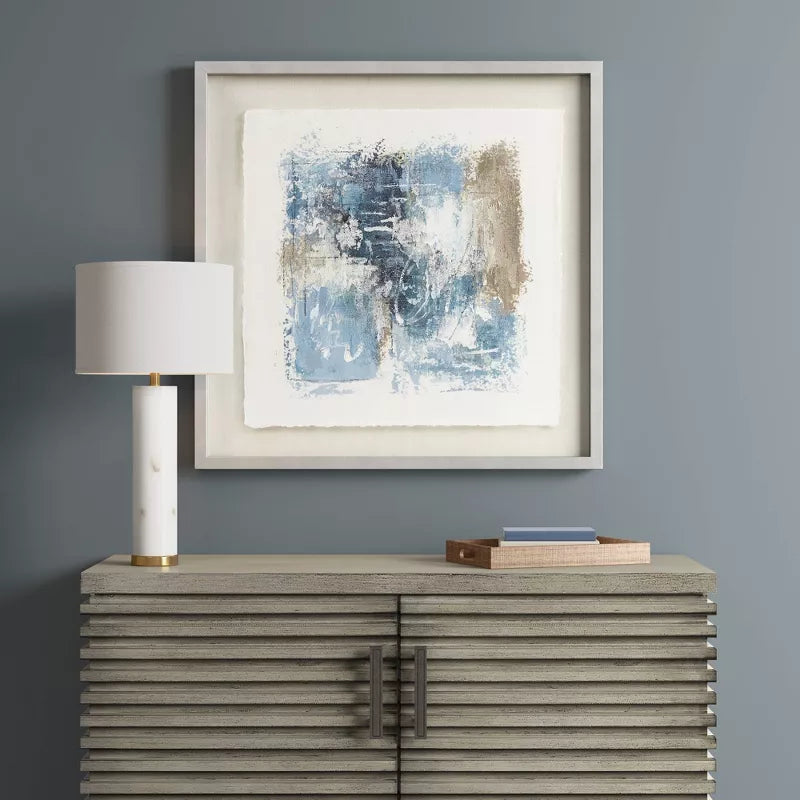 Framed abstract art on a wall above a console table with a lamp and decorative items.
