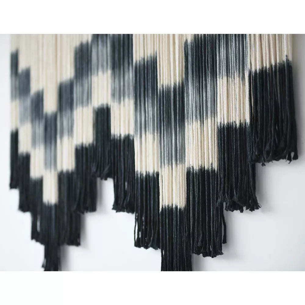 Black and white patterned wall art with fringe on a white background
