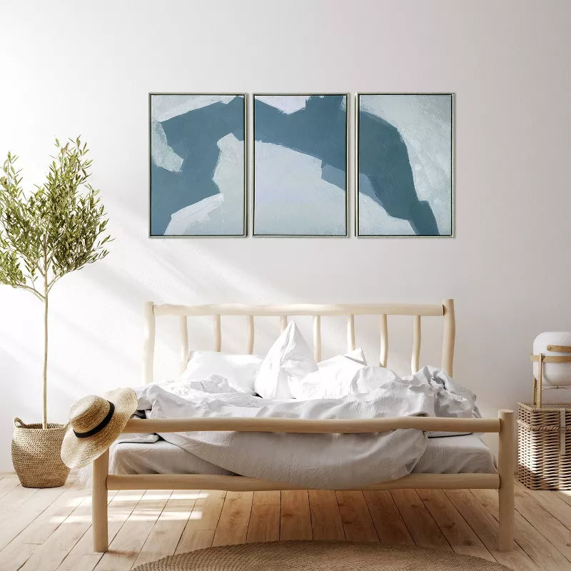 Wooden bed with white bedding in a room with abstract wall art and a plant.