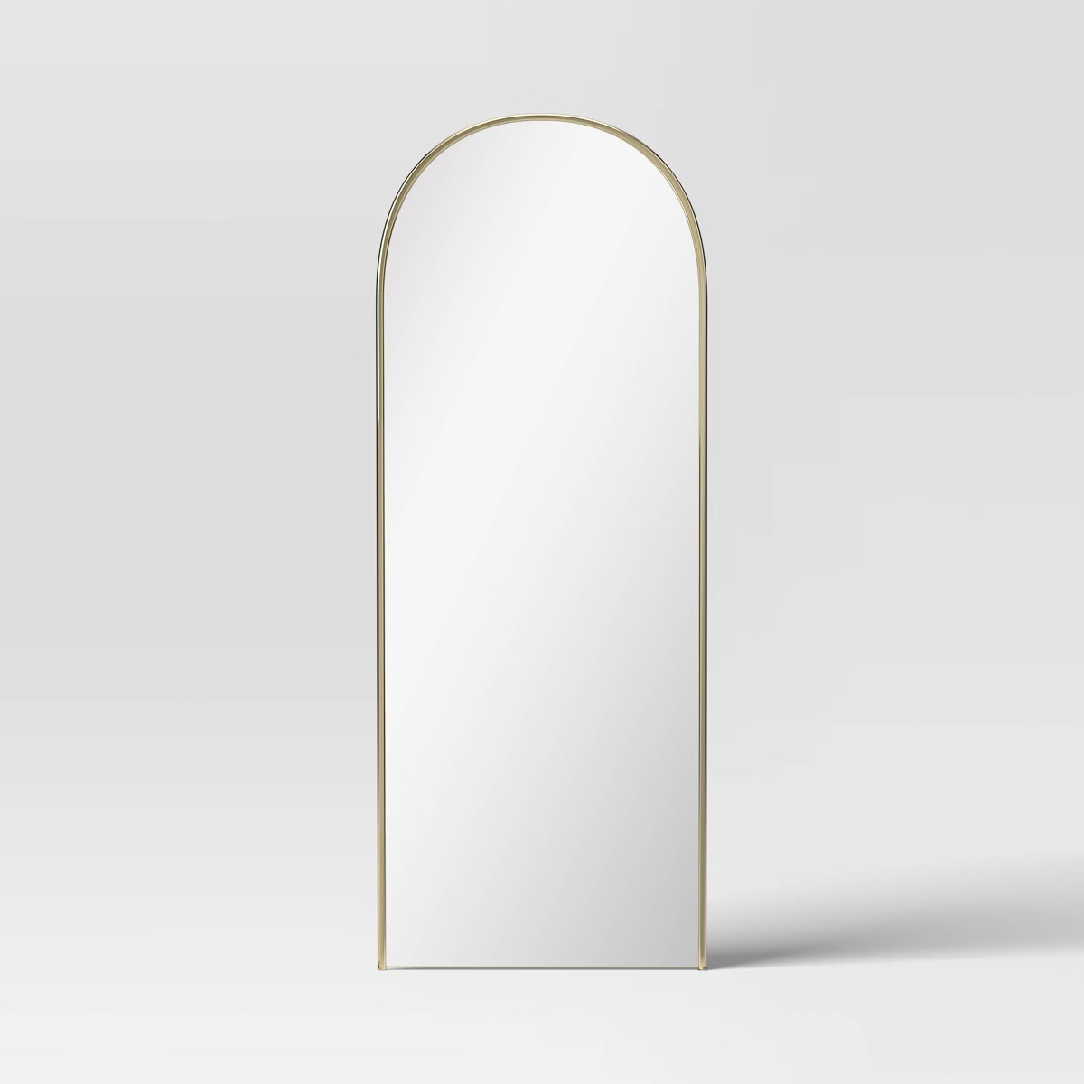 An arched mirror with a thin gold colored frame against a light gray background.