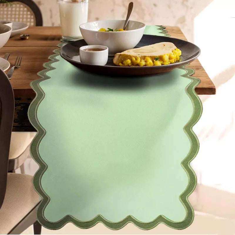 Green scalloped placemat on a dining table with food.