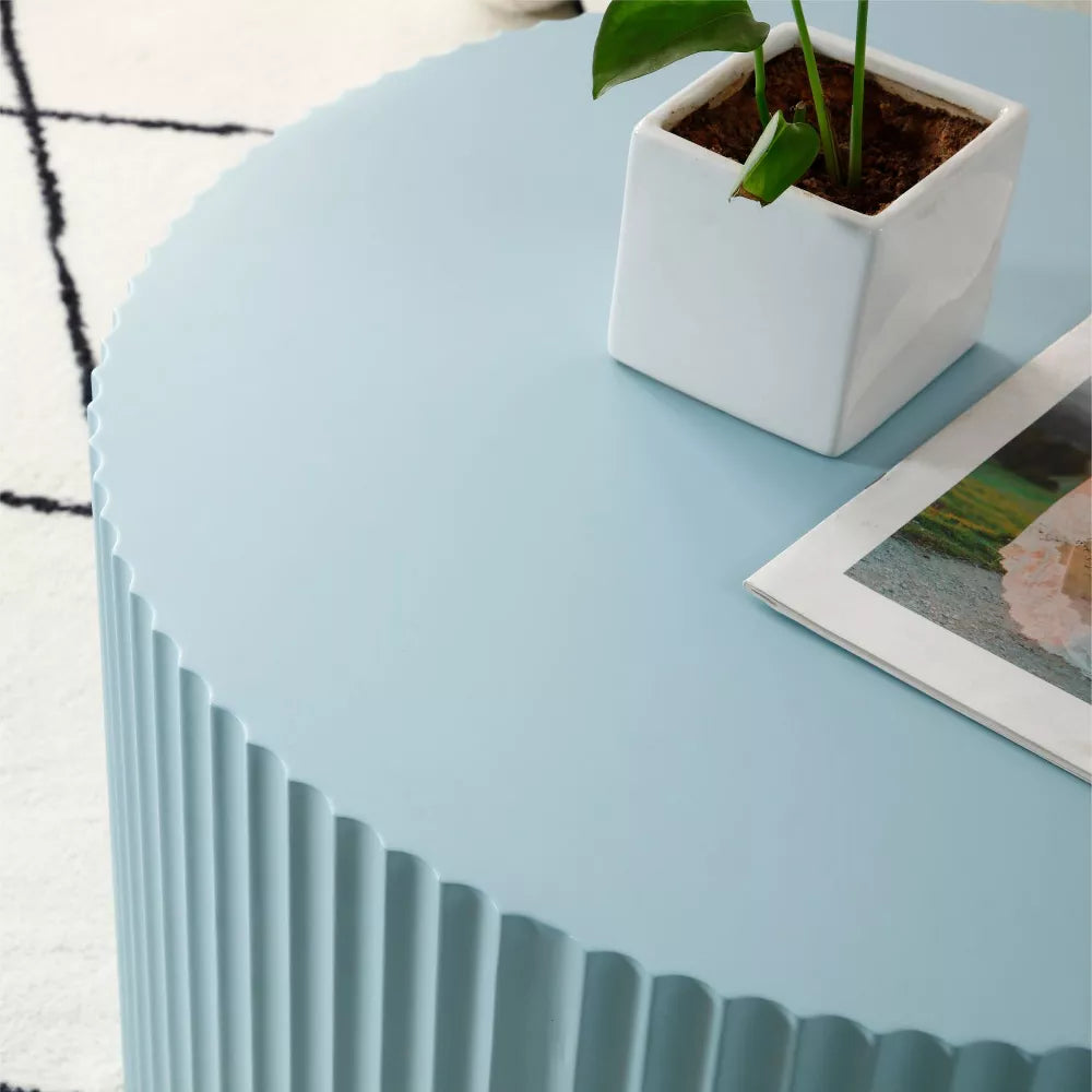 Blue ribbed side table with a magazine on top, featuring a plant and white vase.blue