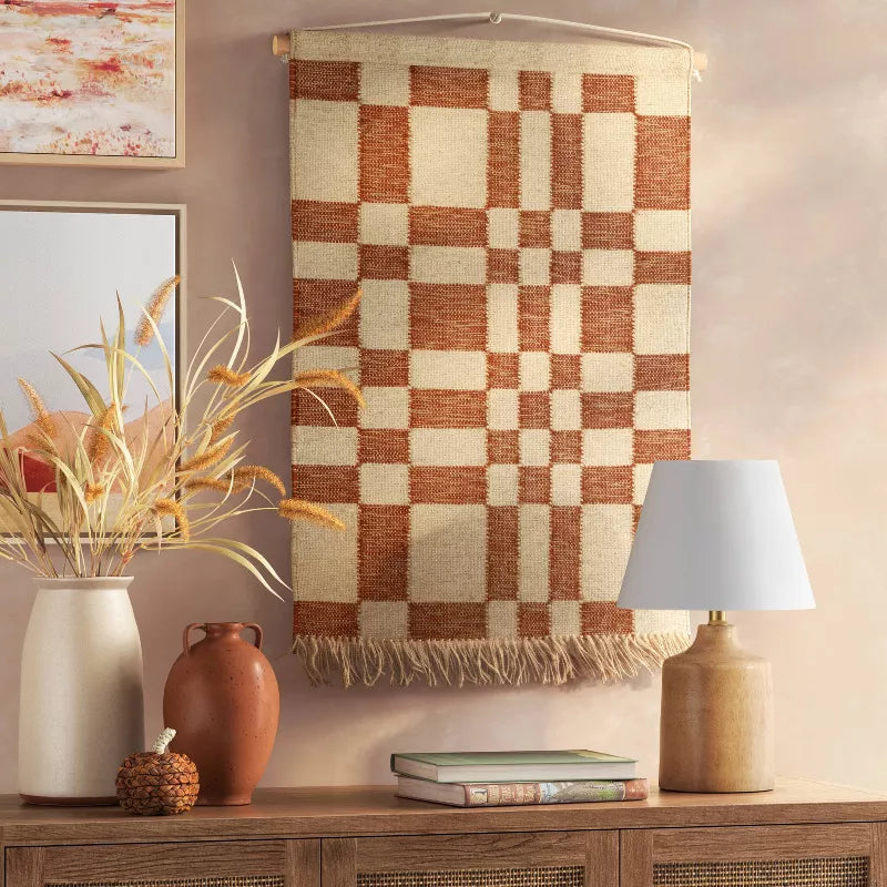 Decorative wall hanging with a checkered pattern above a wooden console table with decorative items.