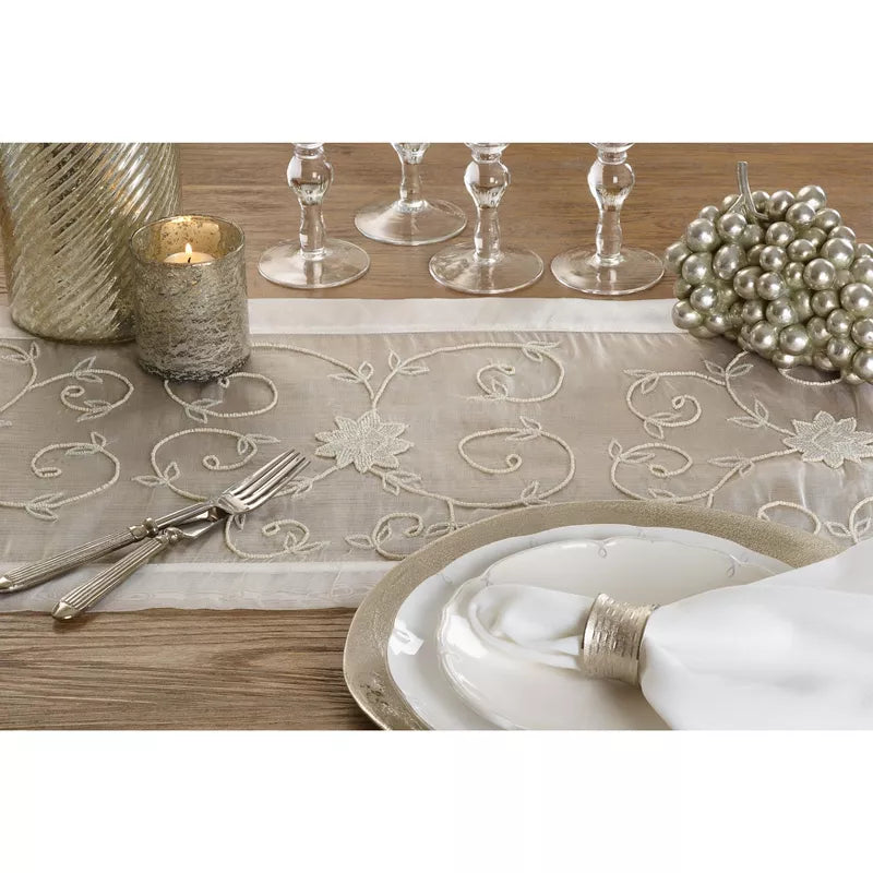 Elegant table setting with embroidered runner, plates, cutlery, and candles on a wooden table.