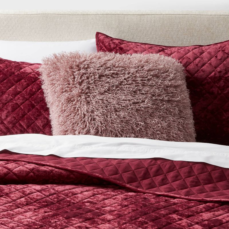 Close-up of a bed with burgundy quilt, pillows, and a fluffy pink pillow. Mauve