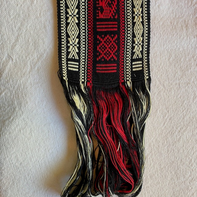 Decorative belt with red, black, and beige patterns on a light background Authentic large woven faja from Cuanajo, Michoacán. Handwoven on a backstrap loom with traditional Purepecha designs. Cotton sash, 54" x 3.5" – wearable or decorative.