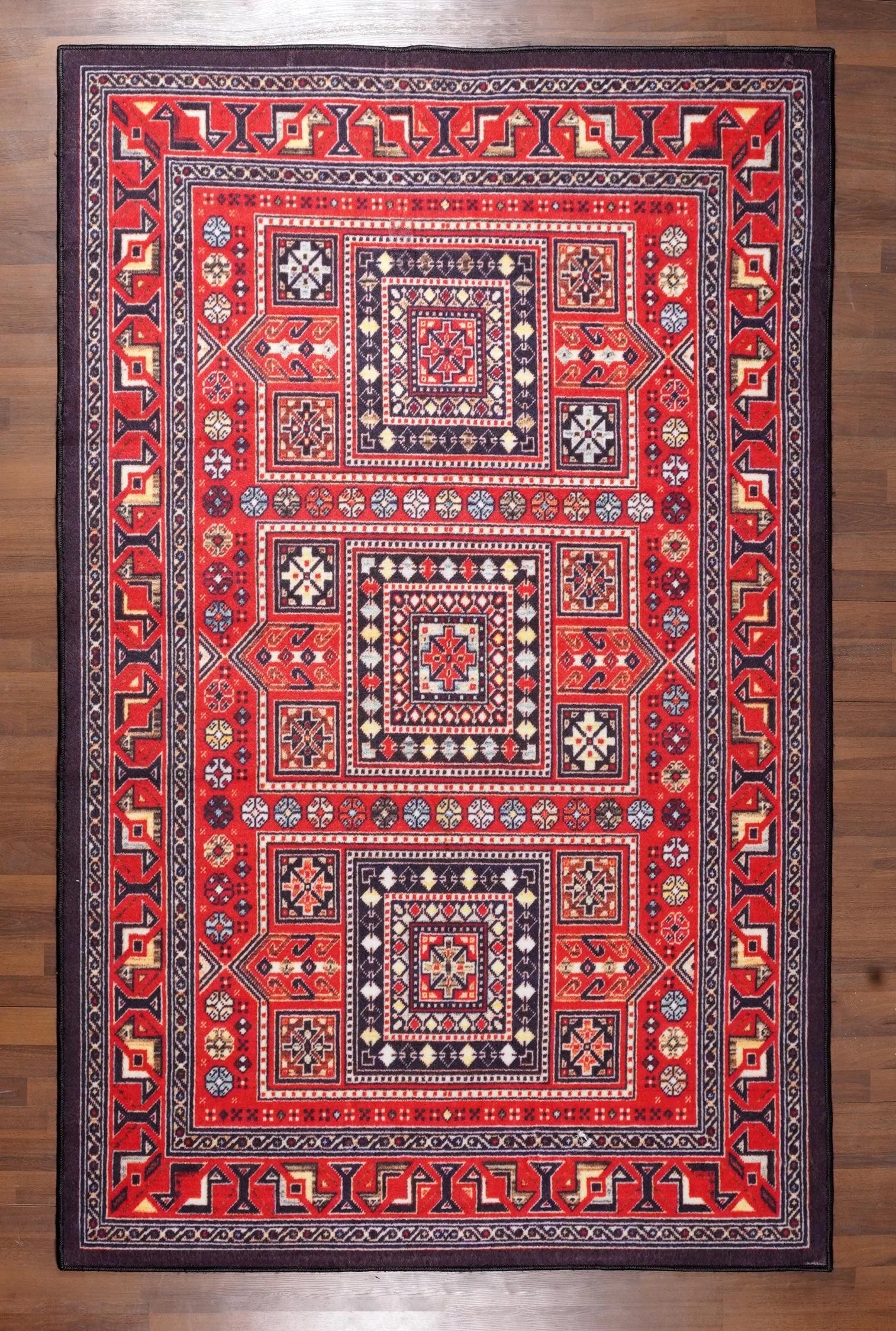 Close-up of a red and black patterned rug on a wooden floor.