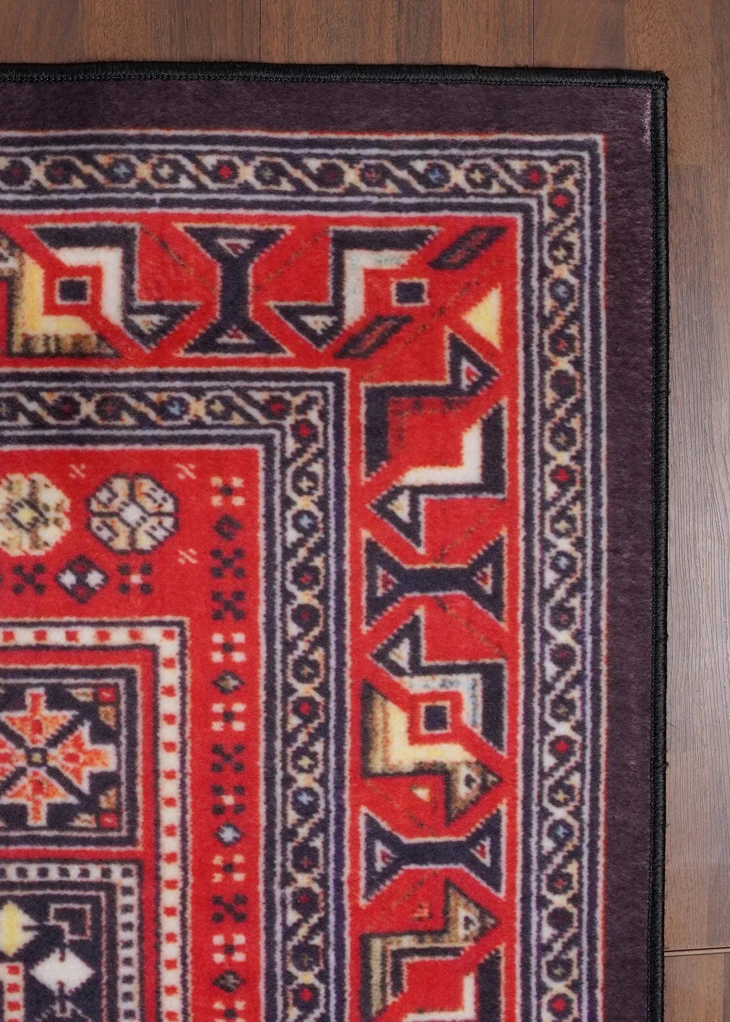 Close-up of a red and black patterned rug on a wooden floor.