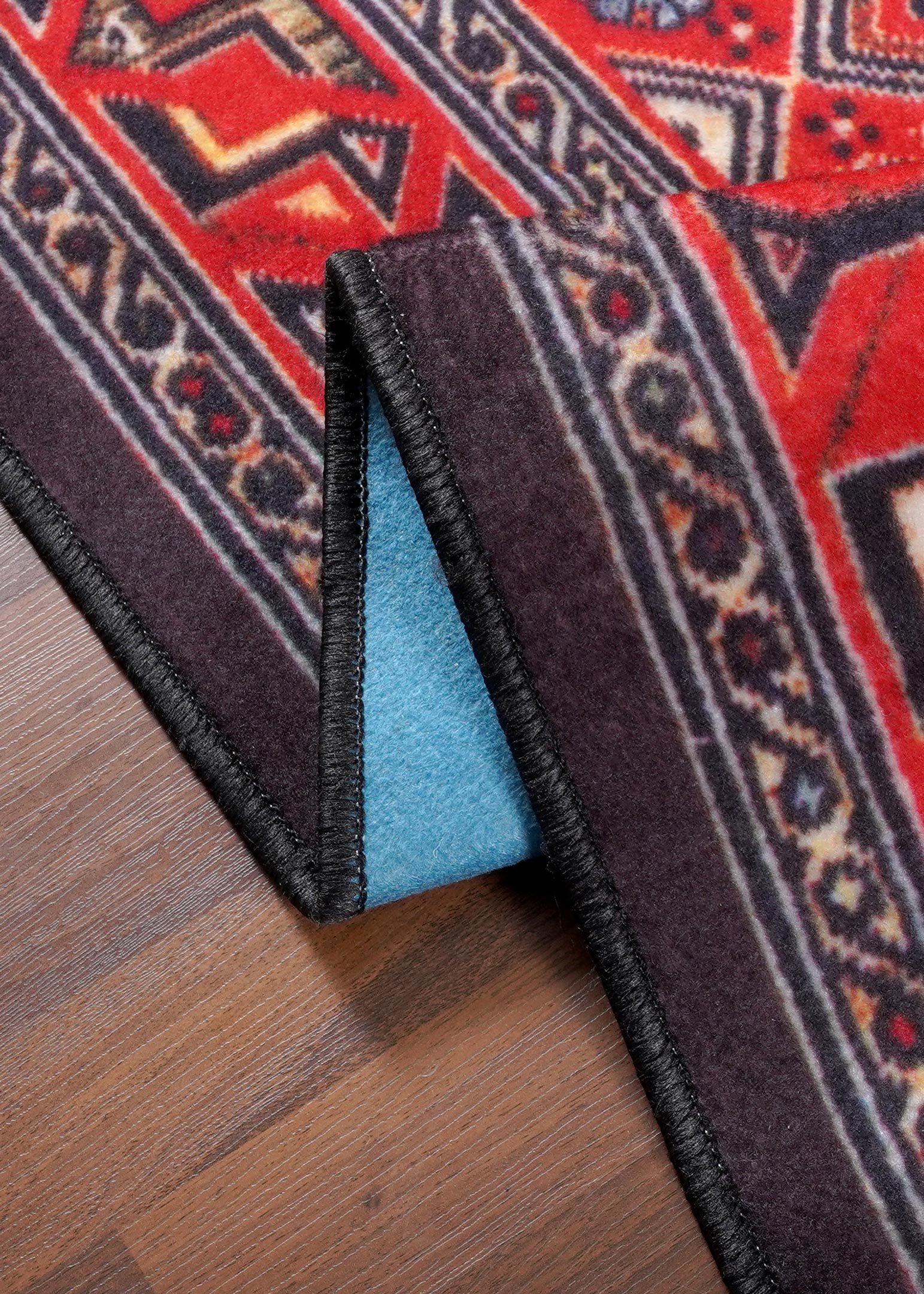 Close-up of a red and black patterned rug on a wooden floor.
