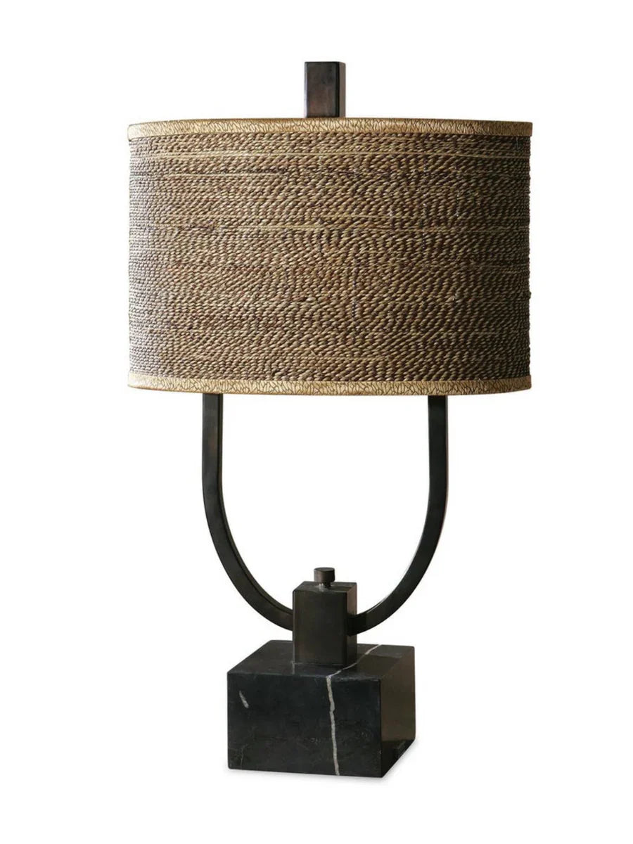 Rustic table lamp with burnished bronze body, black marble base, and a woven rattan oval drum shade with decorative trim.