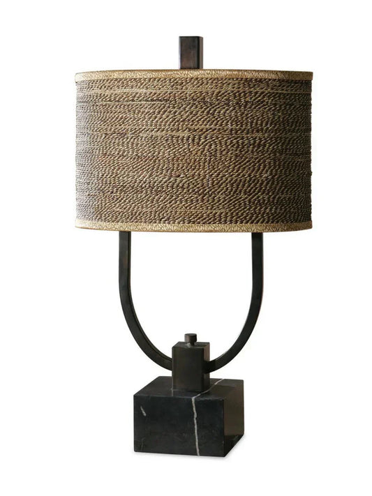 Rustic table lamp with burnished bronze body, black marble base, and a woven rattan oval drum shade with decorative trim.