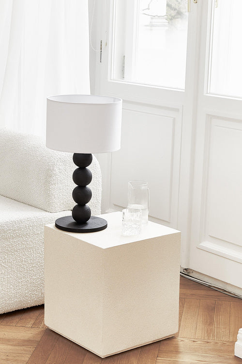 Table lamp with a white shade and black cylindrical base on a light gray background