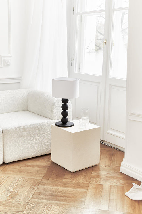 Table lamp with a white shade and black cylindrical base on a light gray background