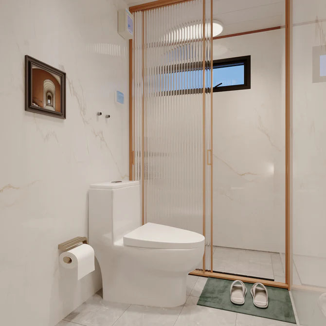 A modern white ceramic toilet in a clean, contemporary bathroom with a glass shower enclosure featuring a bronze frame, marble-look tiled walls, and a small green bath mat on the floor.
