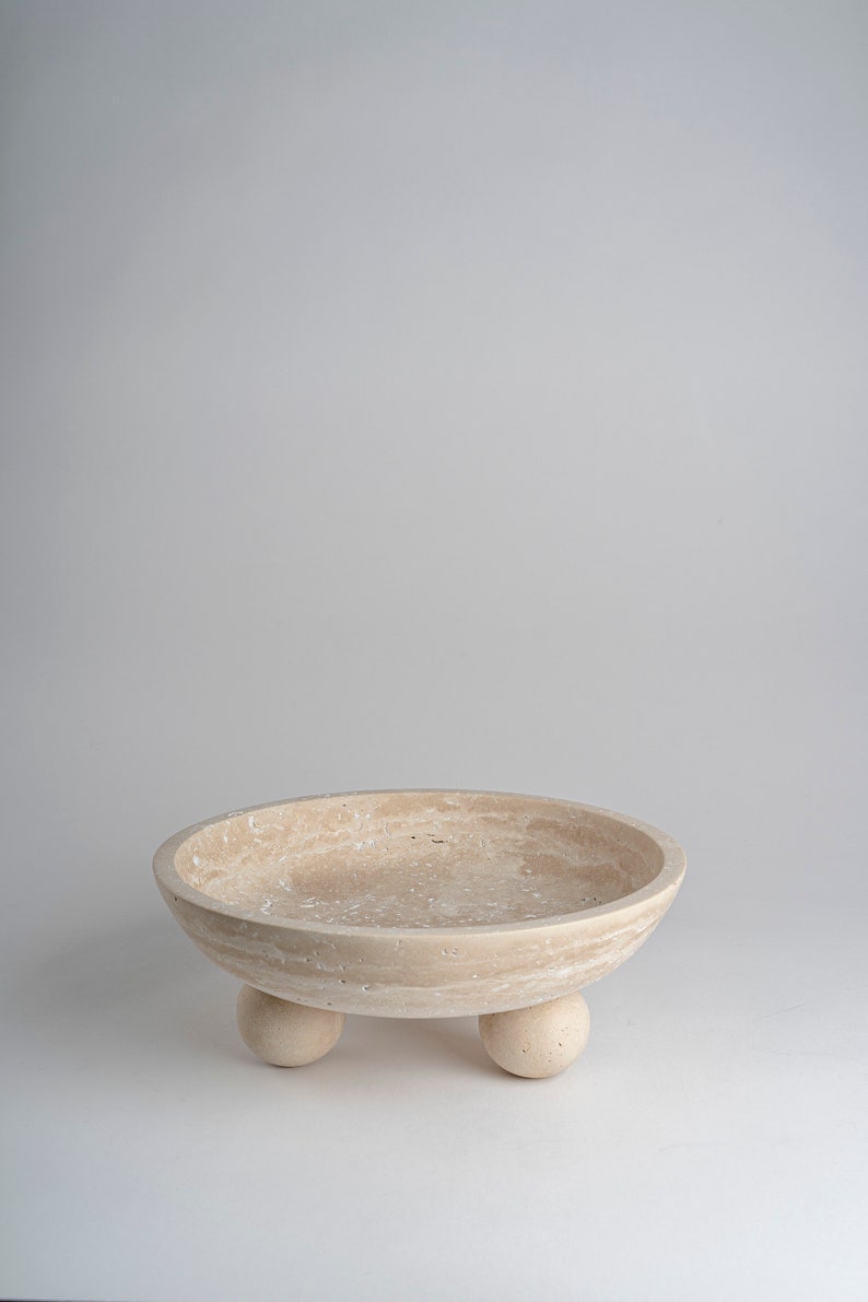 Beige ceramic bowl with three small feet on a light gray background