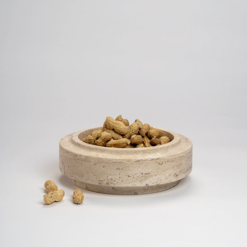 Ceramic bowl filled with peanuts on a light gray background