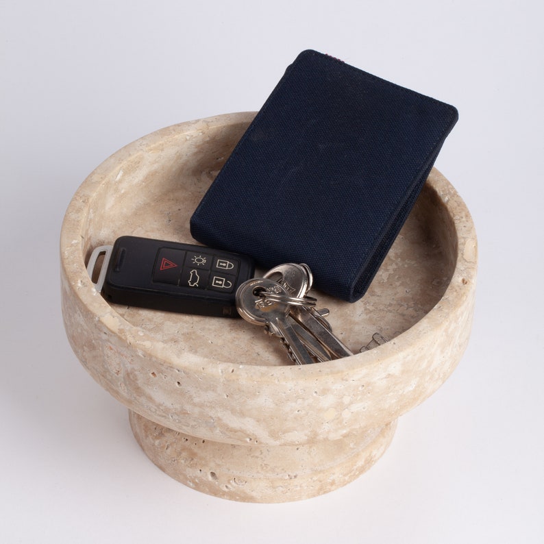 Beige stone bowl with a black wallet and car keys on a white background