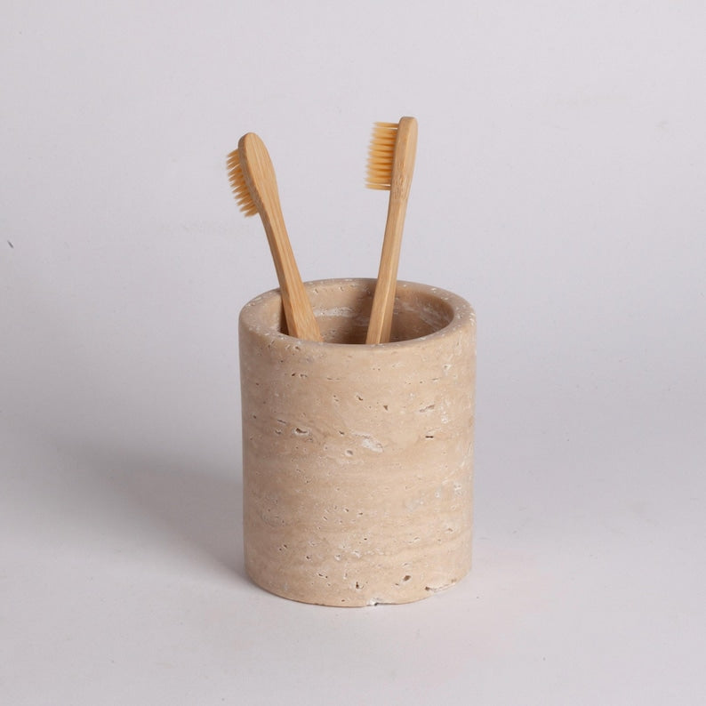 Beige ceramic toothbrush holder with two bamboo toothbrushes on a light gray background