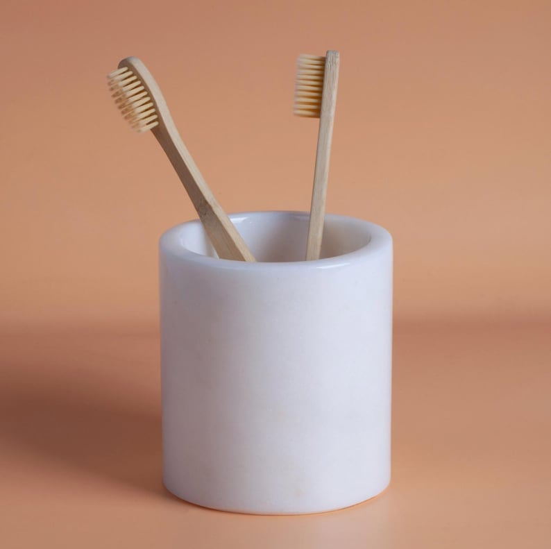 Two wooden toothbrushes in a white ceramic cup on a peach background