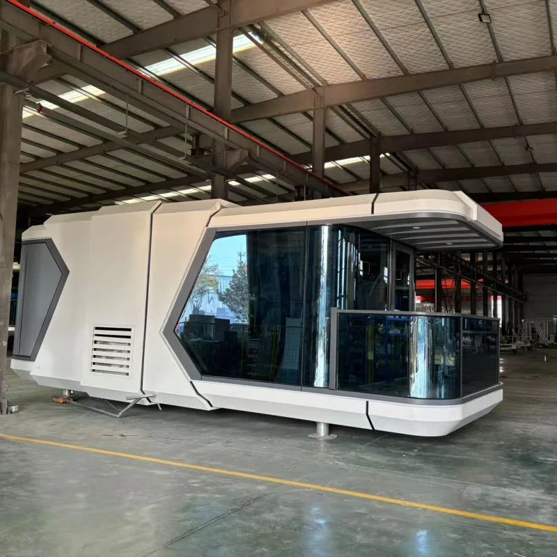 A futuristic white pod-style cabin with large dark-tinted glass windows stands inside a large industrial warehouse or hangar with metal beams and concrete floors.