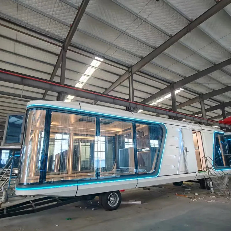 A modern white and blue glass capsule trailer or mobile living unit parked inside a large industrial warehouse with metal beams and skylights.