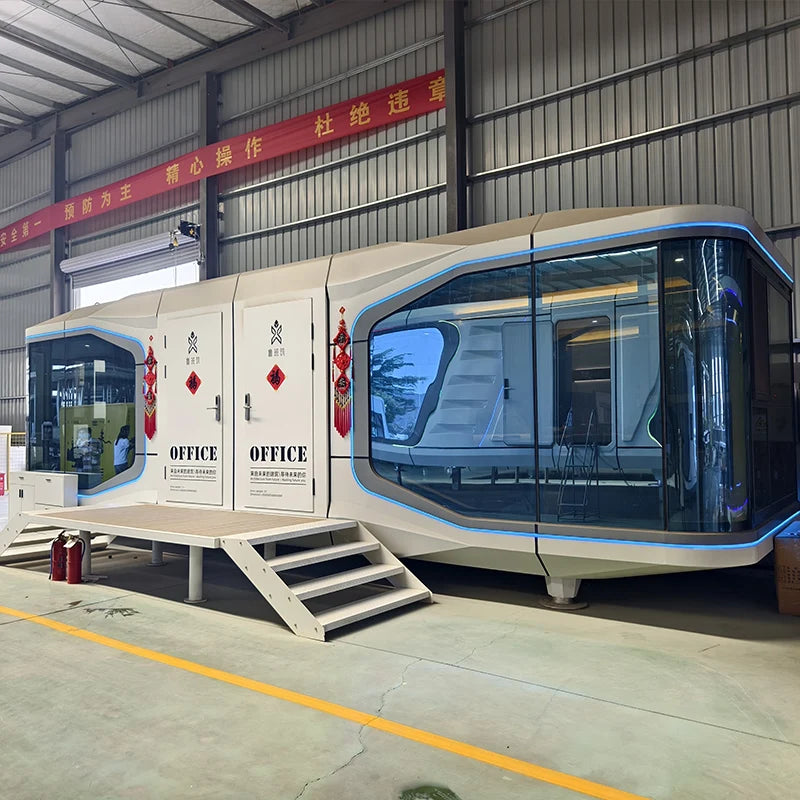 A modern modular office cabin with a futuristic curved design, large glass windows, and blue trim, parked inside a warehouse with metal walls and a concrete floor.