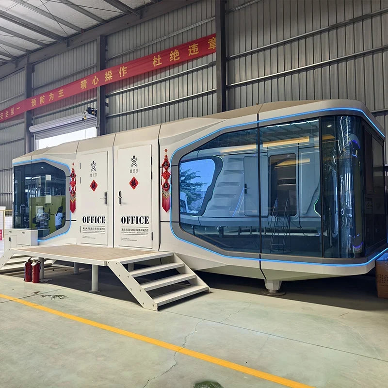 A modern modular office cabin with a futuristic curved design, large glass windows, and blue trim, parked inside a warehouse with metal walls and a concrete floor.