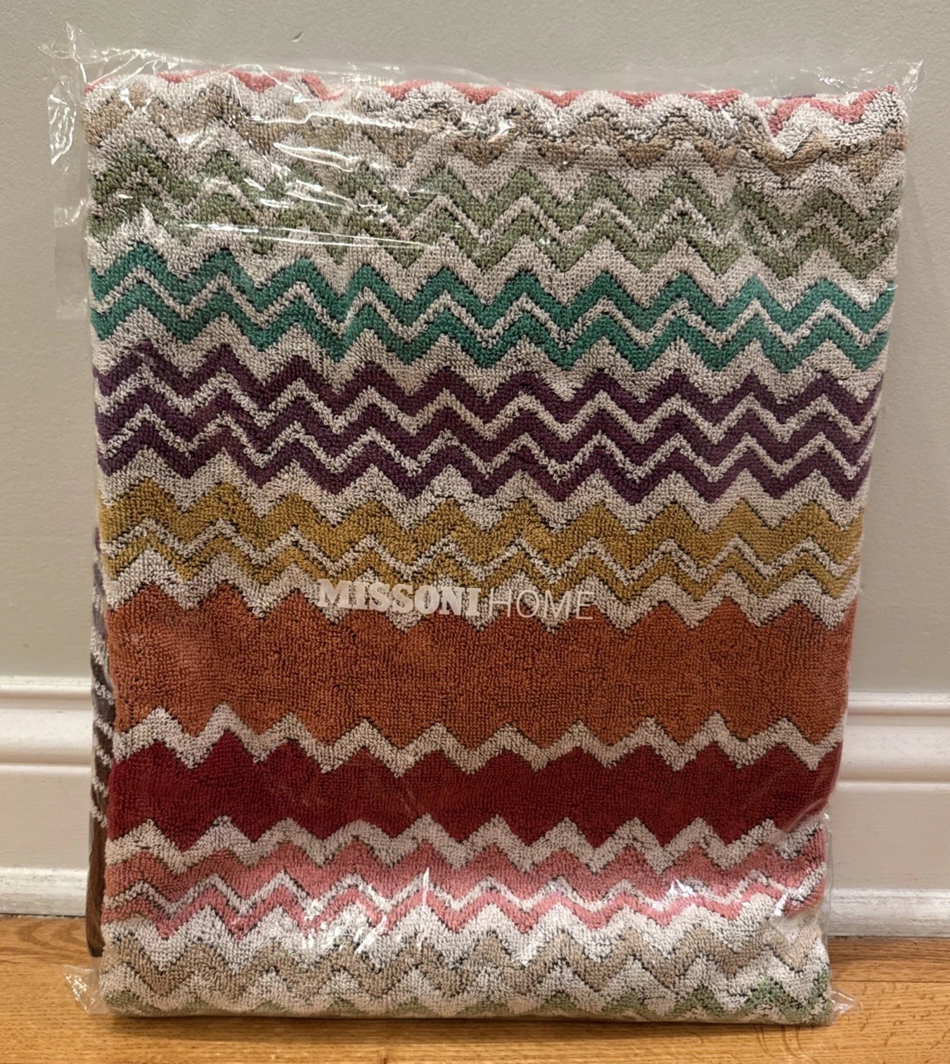 Multicolored zigzag patterned throw blanket with 'Missoni Home' branding on a wooden floor.
