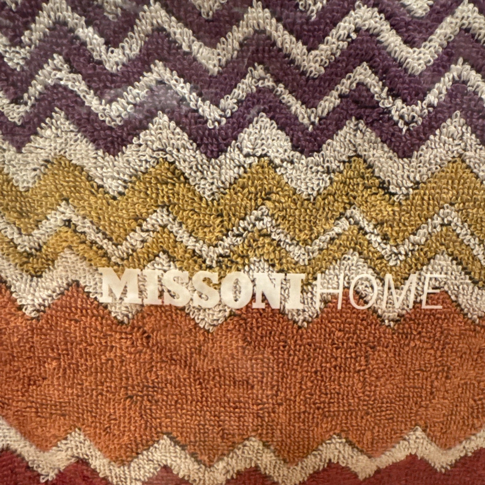 Multicolored zigzag patterned throw blanket with 'Missoni Home' branding on a wooden floor.