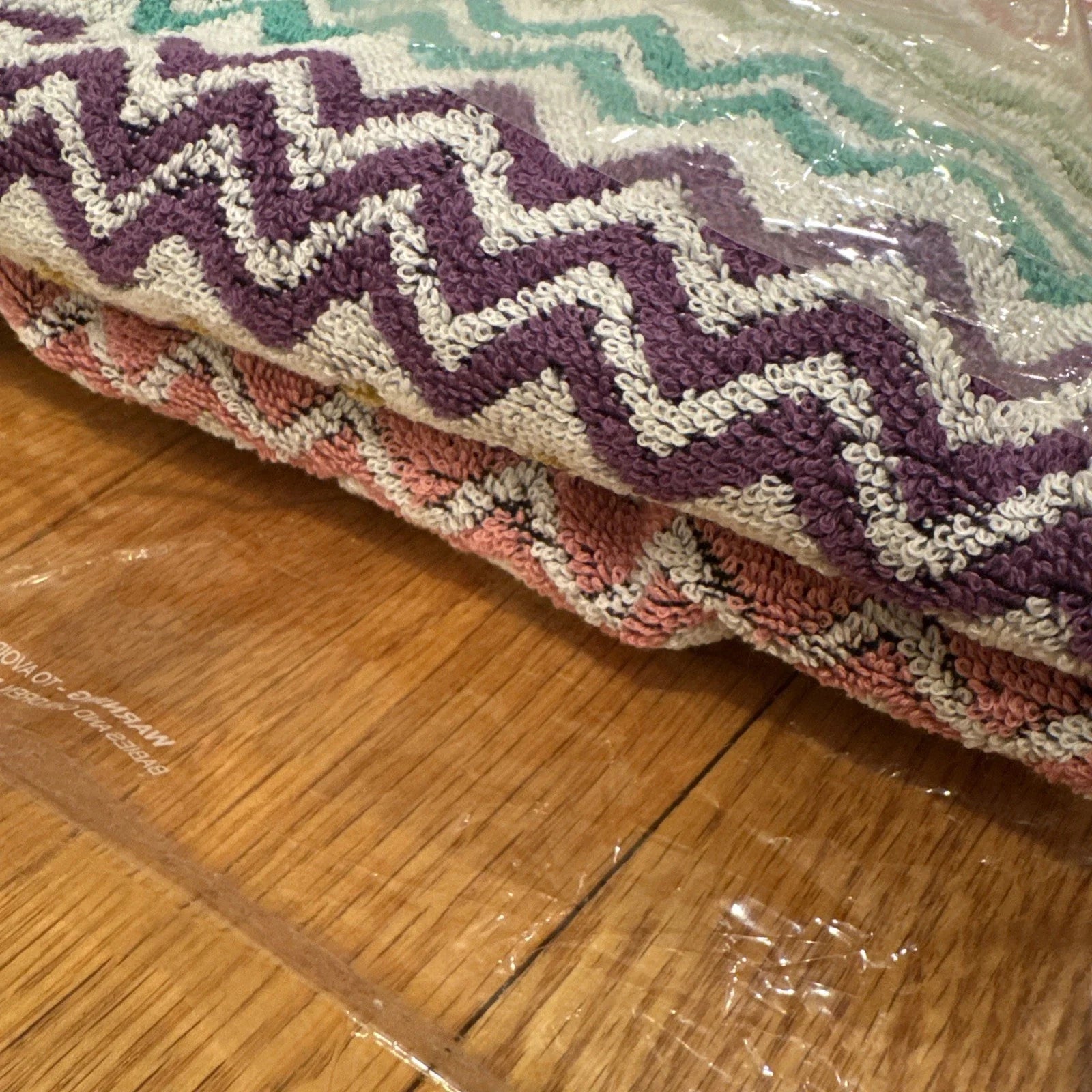 Multicolored zigzag patterned throw blanket with 'Missoni Home' branding on a wooden floor.