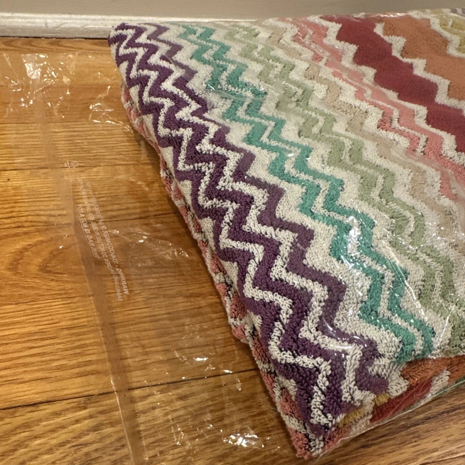 Multicolored zigzag patterned throw blanket with 'Missoni Home' branding on a wooden floor.