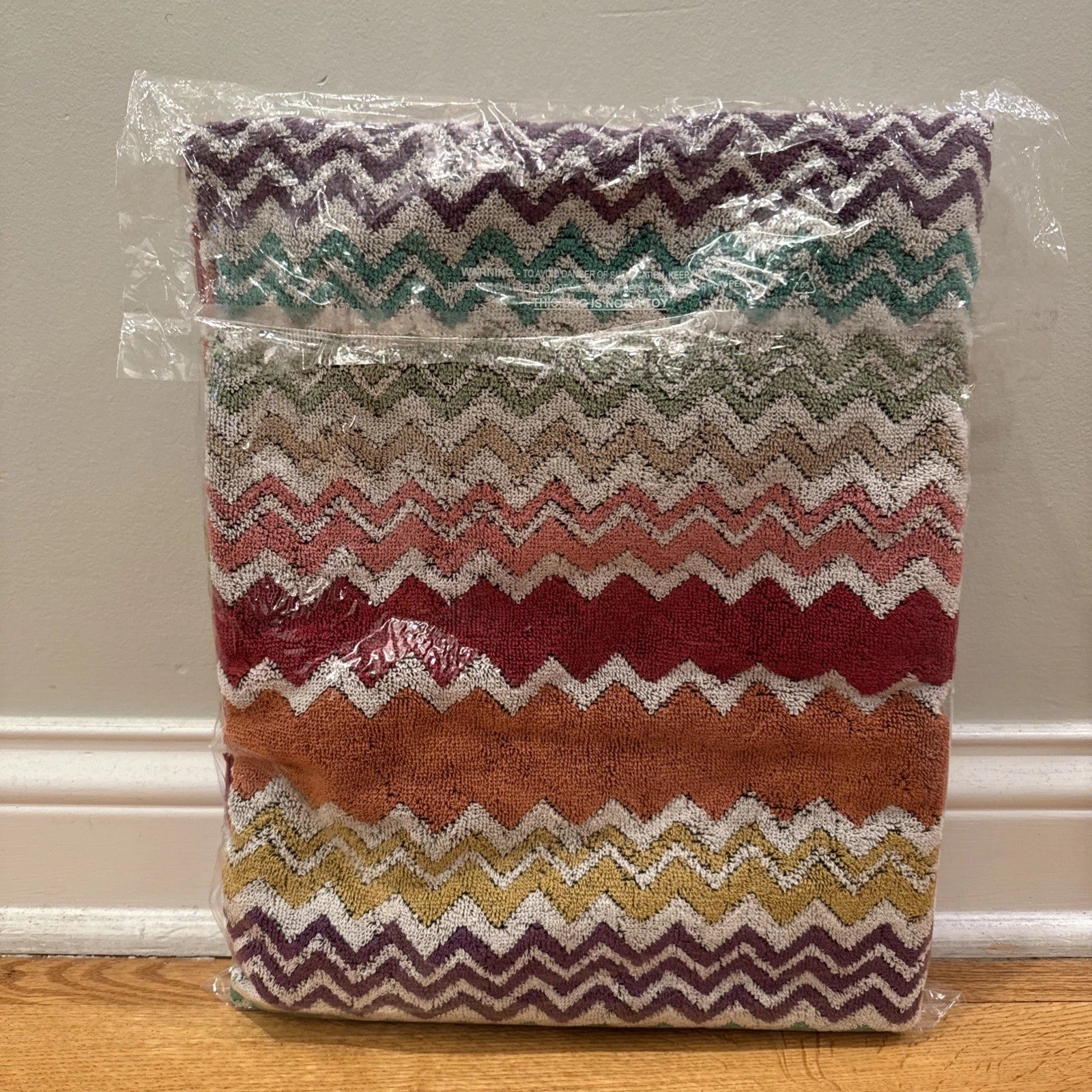 Multicolored zigzag patterned throw blanket with 'Missoni Home' branding on a wooden floor.