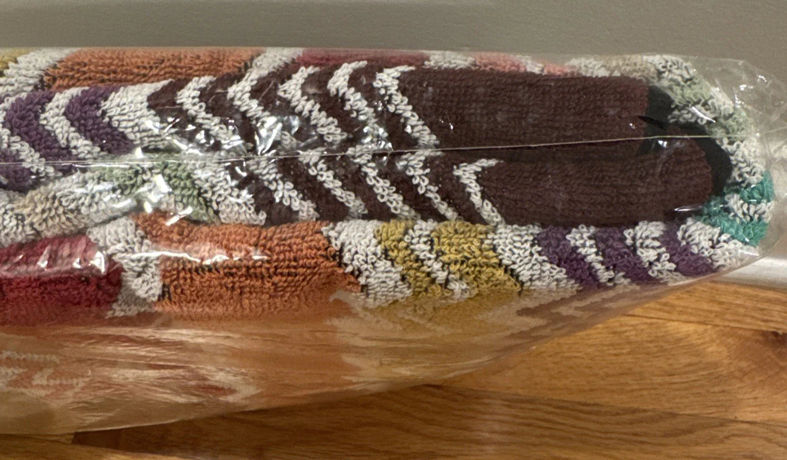 Multicolored zigzag patterned throw blanket with 'Missoni Home' branding on a wooden floor.