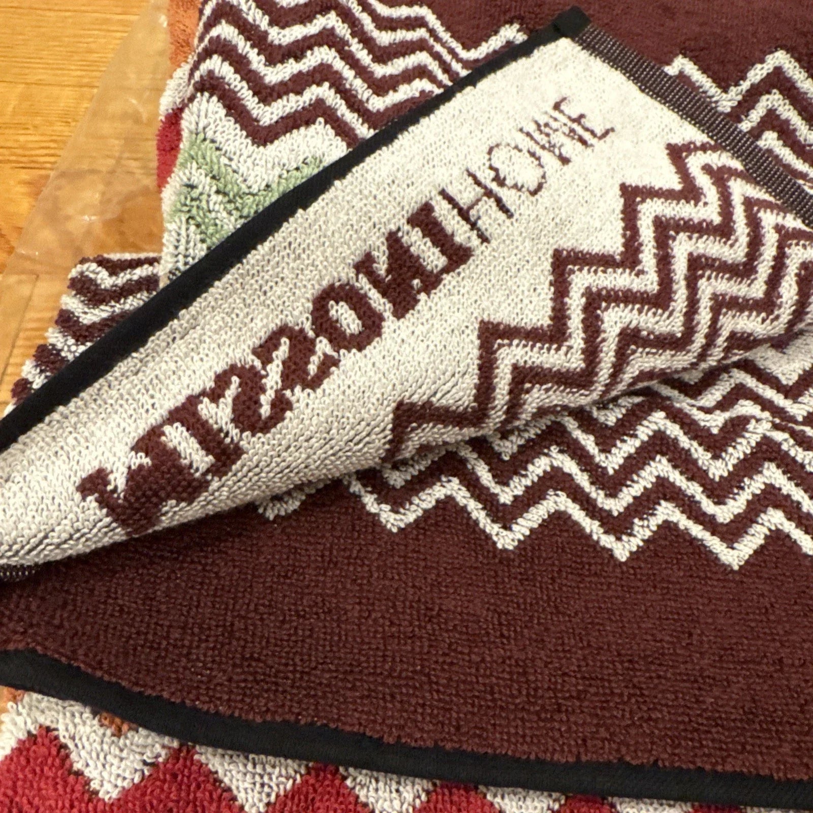 Multicolored zigzag patterned throw blanket with 'Missoni Home' branding on a wooden floor.